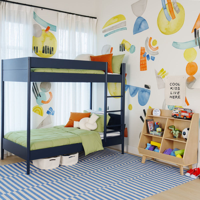 Modern kids' bedroom with navy bunk bed, green bedding, colorful abstract wall mural, wooden toy storage shelf and striped blue rug