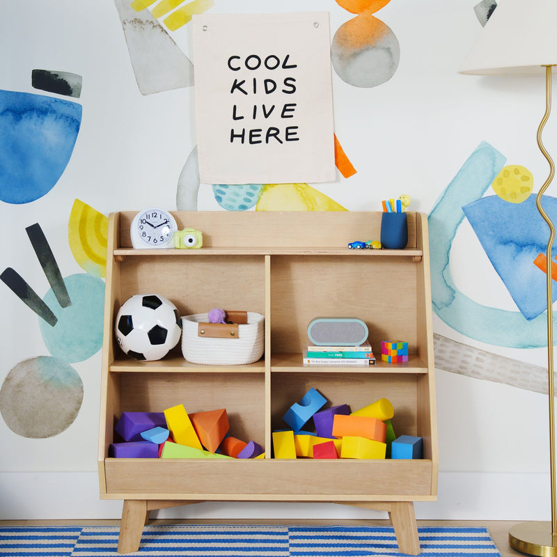 Kids playroom wooden cubby shelf with 'Cool Kids Live Here' wall banner, colorful foam blocks, soccer ball, clock and lamp