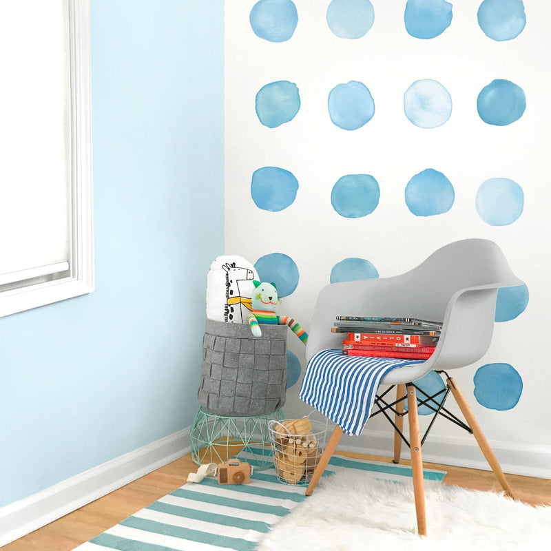 Kids nursery corner with blue watercolor polka dot wall decals, modern gray Eames-style chair, striped teal rug, toy basket and stuffed animals