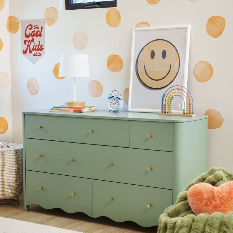 Kids bedroom with sage green dresser, white lamp, blue alarm clock, wooden abacus, smiley face print and orange polka-dot wall