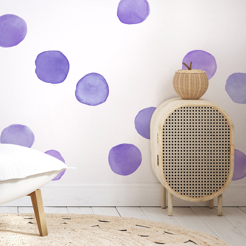 Boho Scandinavian nursery corner with purple watercolor polka-dot wall decals, rattan cane cabinet, wicker apple basket and white linen chair