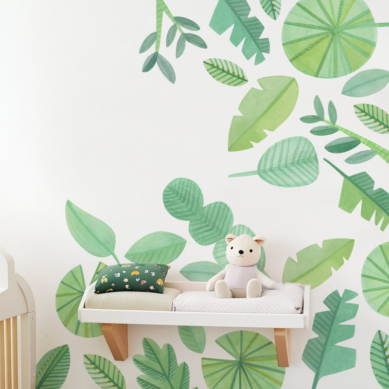 Nursery changing shelf with plush teddy bear, green tropical leaf wall mural and patterned pillow, baby room decor