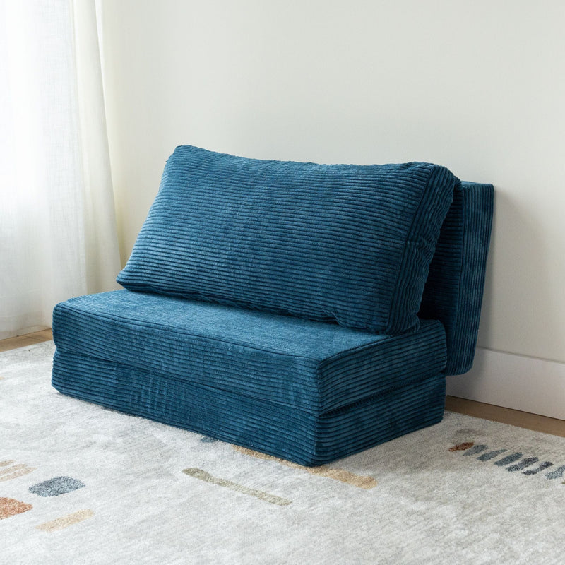 Blue corduroy convertible floor chair folded into compact sofa, modern small-space seating on a patterned rug next to white wall and curtain