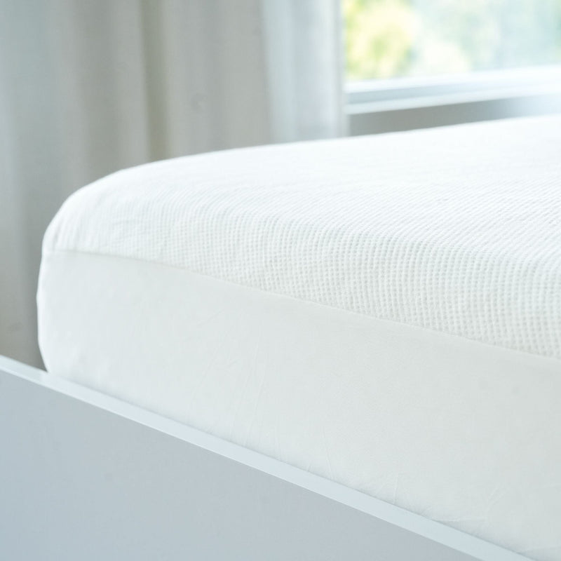 Close-up of a comfortable white mattress in a modern bedroom setting with ambient natural light.