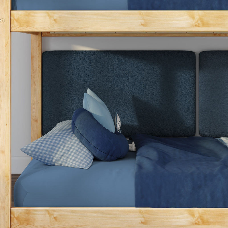 Lower bunk of wooden kids' bunk bed with navy textured headboard, blue gingham pillow, round navy cushion and blue blanket in a cozy children's bedroom