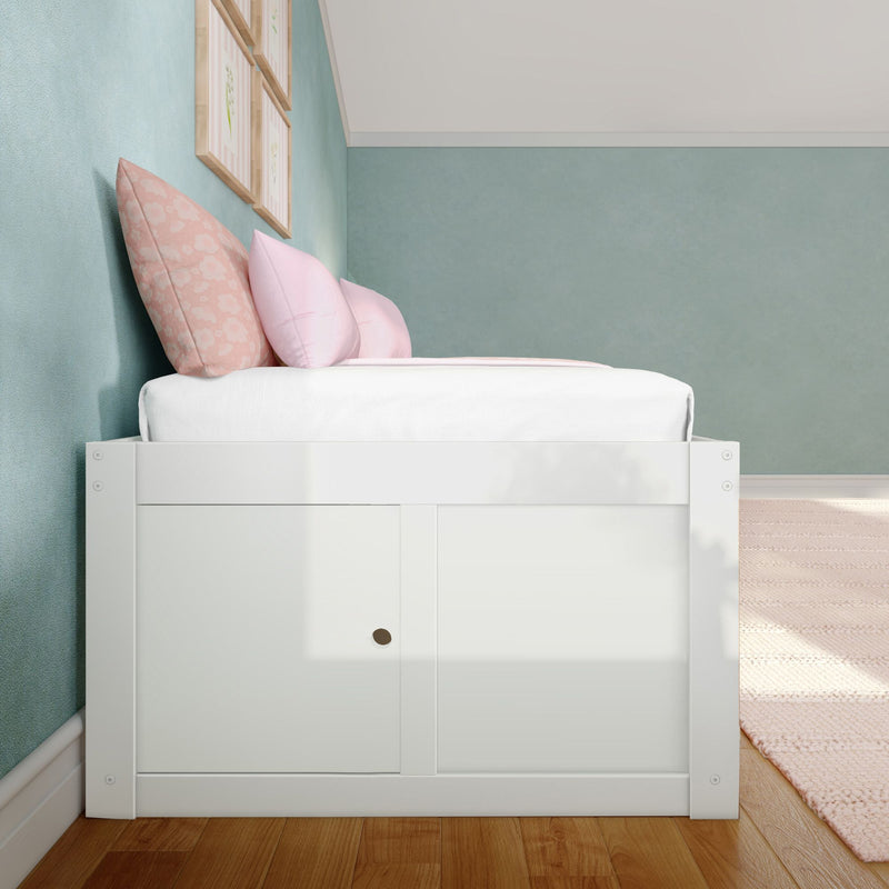 Cozy pastel bedroom with white storage bed, pink floral and blush pillows, teal textured accent wall, framed floral prints and hardwood floor
