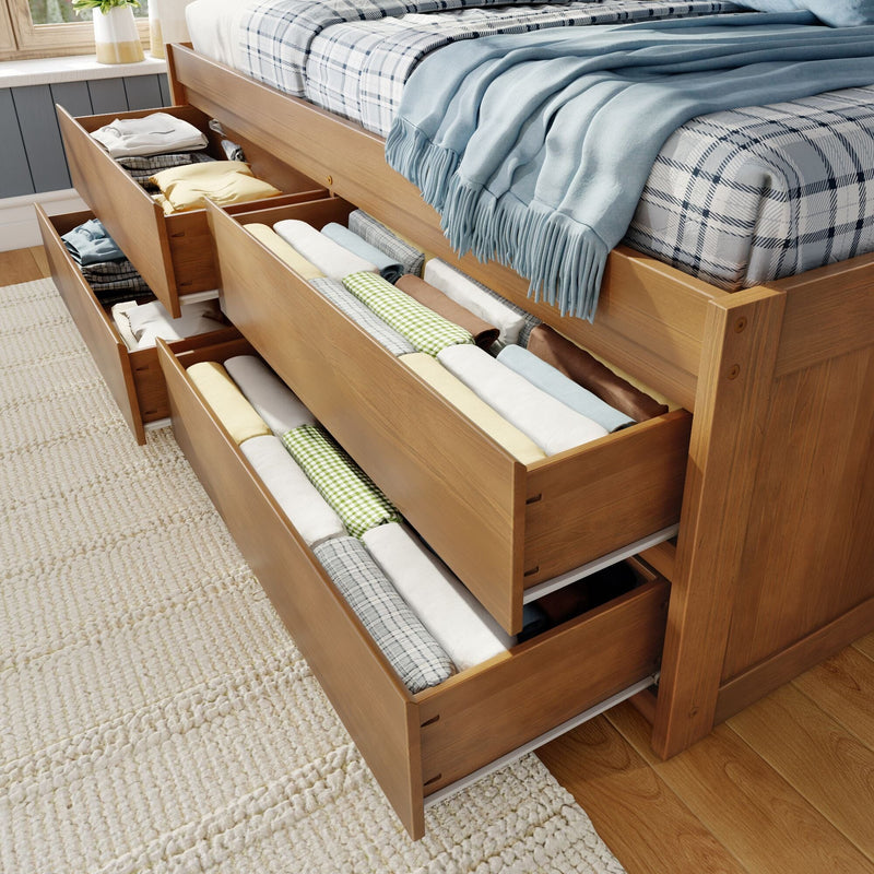 Wooden storage bed with pull-out under-bed drawers neatly organized with folded linens and a blue throw blanket