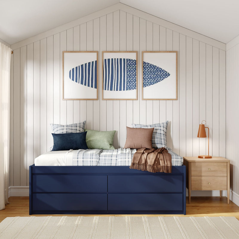 Coastal bedroom with navy storage bed, plaid bedding and pillows, shiplap paneled wall with three framed blue surfboard prints, wooden nightstand and orange bedside lamp