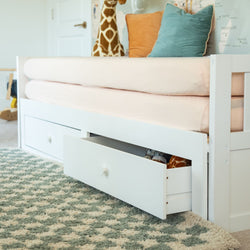 White kids daybed with pull-out under-bed storage drawers, pink fitted sheet, giraffe stuffed animal and teal and orange pillows on a green patterned nursery rug