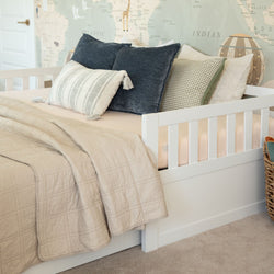 White wooden daybed in children's nursery with neutral beige quilt, textured pillows, wicker basket, and world map wallpaper