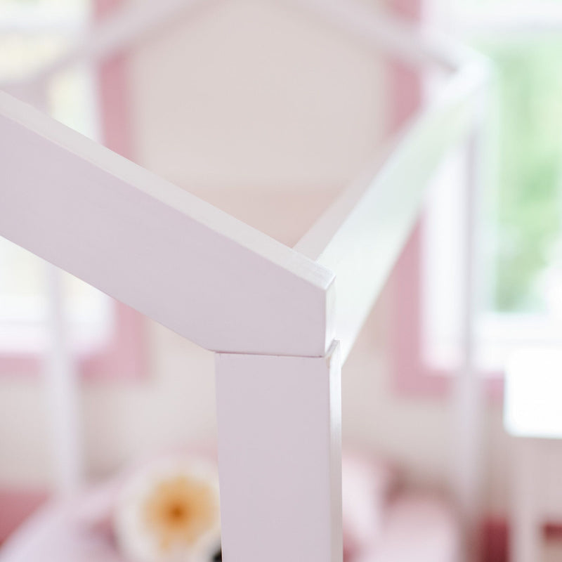 Close-up of white painted wooden crib railing in a pastel pink baby nursery, soft-focus interior with blurred floral accent and nursery decor