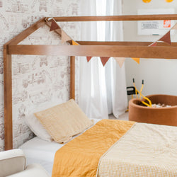 Children's bedroom with a wooden canopy bed, yellow bedding, and construction-themed wallpaper.