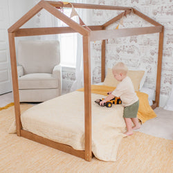Toddler playing with toy truck on canopy bed in nursery with construction-themed wallpaper.