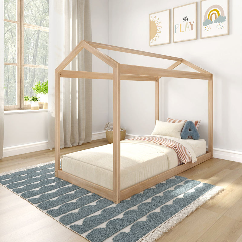 Scandinavian-style kids bedroom with natural wood house-frame bed, neutral bedding, blue patterned rug, window plants and playful framed wall art