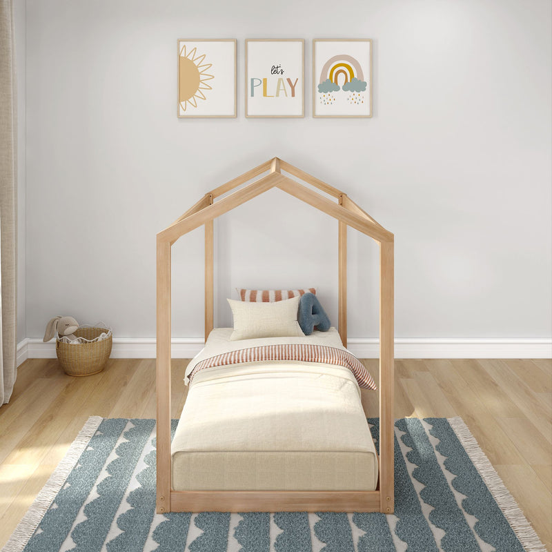 Neutral nursery and kids room with wooden house-frame toddler bed, beige bedding, blue patterned rug, wicker toy basket and playful sun and rainbow wall art saying "let's play