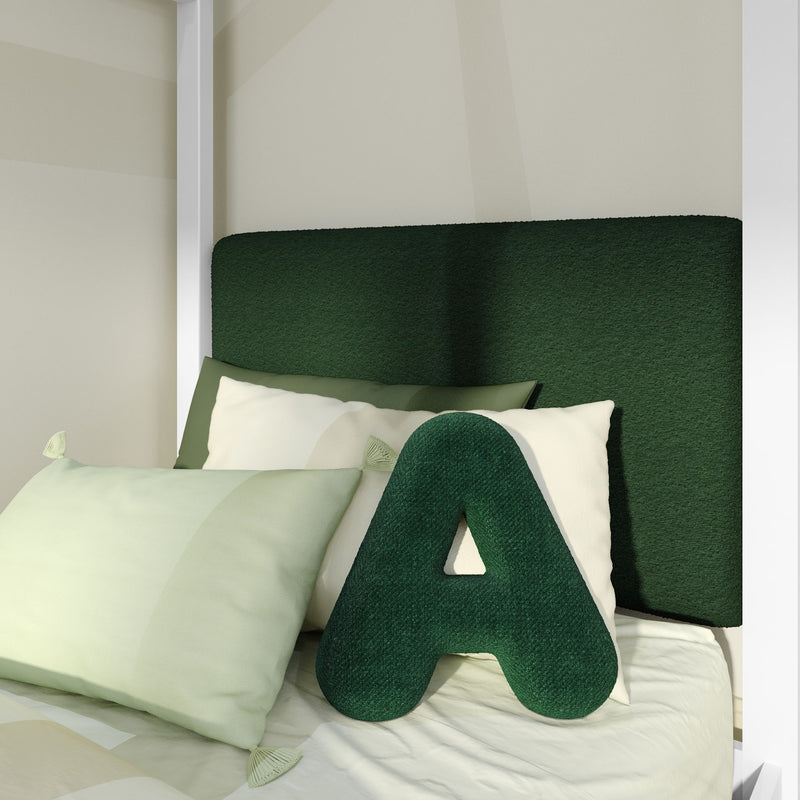 Close-up of modern bedroom with dark green upholstered headboard, green letter “A” decorative pillow and light green bedding