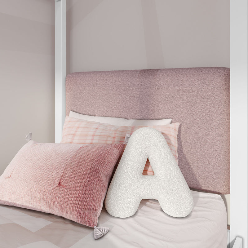 Pink upholstered headboard with textured blush pillows, pastel plaid pillowcase and white A-shaped decorative cushion in a cozy modern girls' bedroom