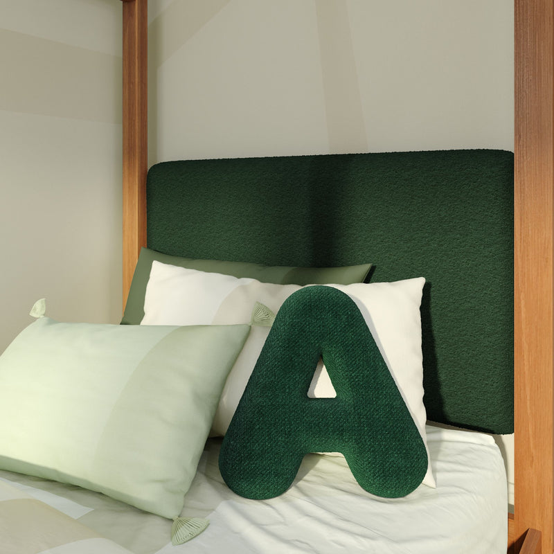 Close-up of modern bedroom with dark green textured upholstered headboard, wooden bed frame posts, green A-shaped accent pillow and pale green pillows