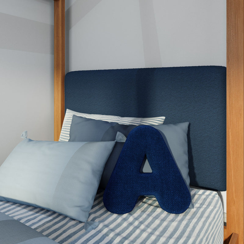 Close-up of modern navy upholstered headboard with decorative navy letter A cushion, assorted blue pillows, striped bedding and wooden bed frame