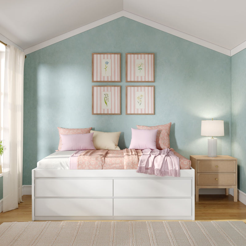 Cozy pastel bedroom with mint green accent wall, white storage daybed with pink bedding, wooden nightstand and table lamp, framed botanical prints
