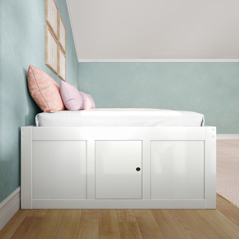 White wooden storage bed with pastel pink and peach pillows against a mint green wall and framed art in a cozy kids' bedroom nursery