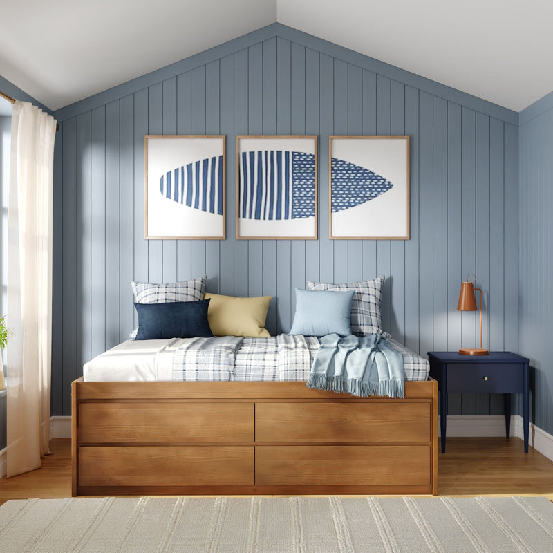 Coastal bedroom with blue vertical shiplap wall, wooden platform bed with storage drawers, plaid bedding and mixed blue and yellow pillows, triptych blue artwork and navy nightstand with copper lamp