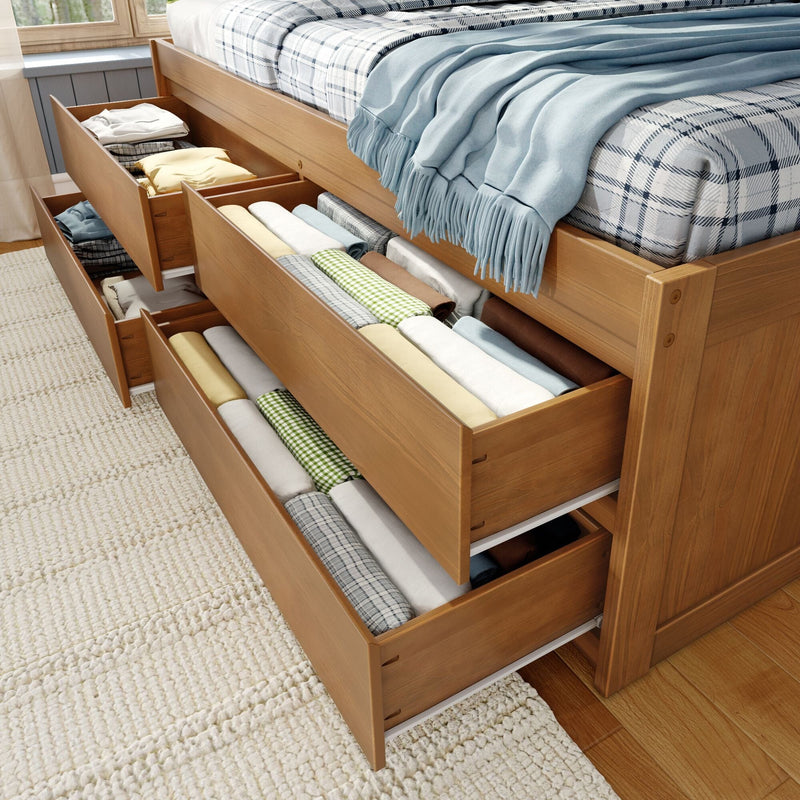 Wooden bed with under-bed storage drawers neatly organized with folded linens, blankets and throws — space-saving bedroom storage solution