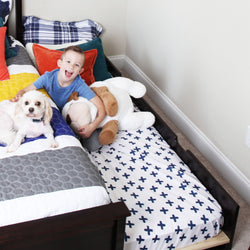 Child smiling on a colorful bed with a cute dog and stuffed animal, highlighting family-friendly bedroom decor.
