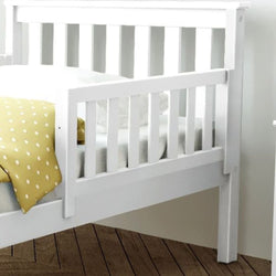 White wooden toddler bed with safety rail and yellow polka dot blanket on a wooden floor.