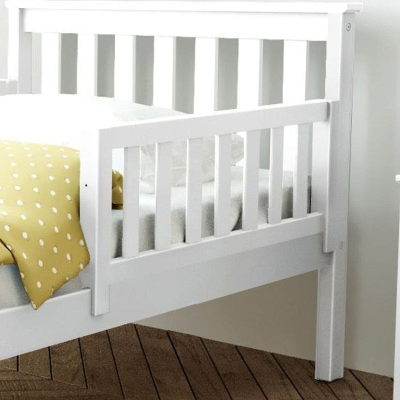 White wooden toddler bed with safety rail and yellow polka dot blanket on a wooden floor.