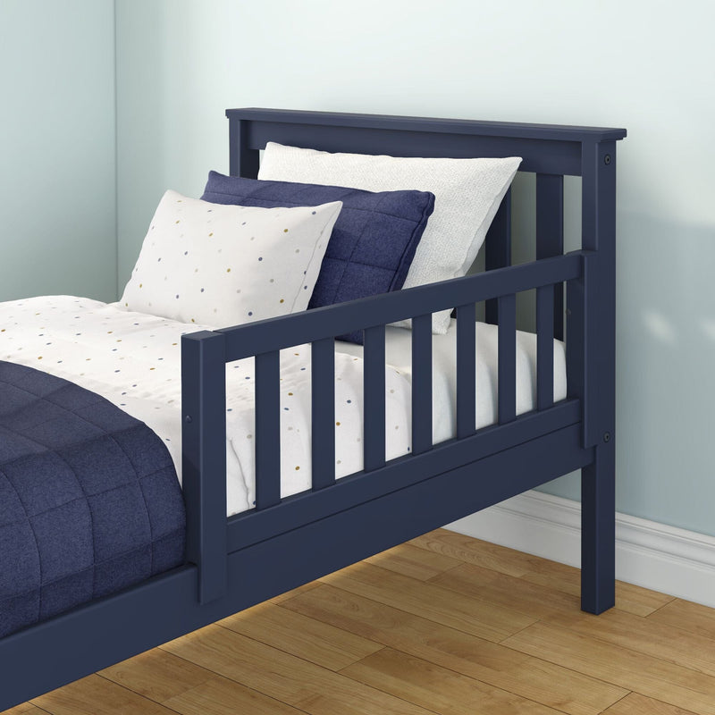 Navy blue wooden toddler bed with safety guardrail, navy quilt and white polka-dot sheets in a kids bedroom with light blue walls and hardwood floor
