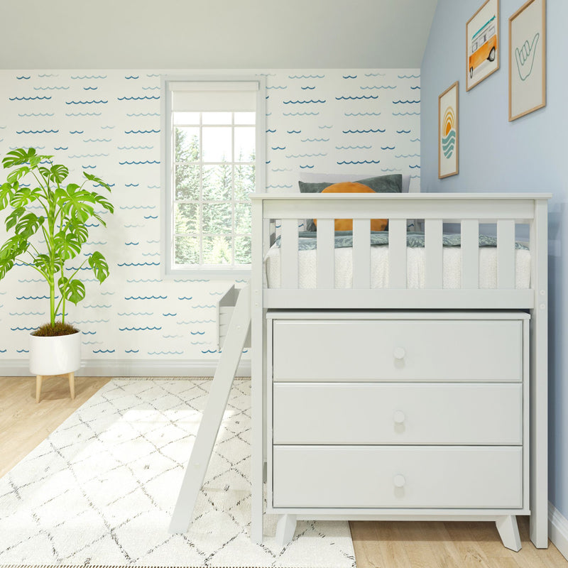 Modern coastal nursery with white loft crib, blue wave-pattern wallpaper, framed ocean-themed prints, green potted plant and white storage dresser