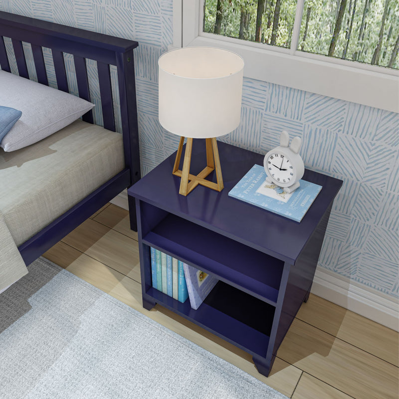 Navy blue nightstand in a children's bedroom with a wooden tripod bedside lamp, white bunny alarm clock and "The Tale of Peter Rabbit" book against blue patterned wallpaper and a matching navy bed frame