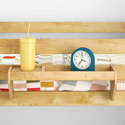 Wooden bed shelf with a yellow cup and alarm clock, colorful bedspread background.