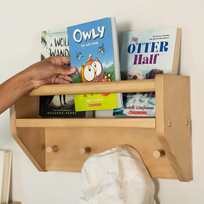 Child's hand reaching for a book on a wooden shelf with other children's books.