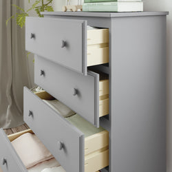Gray wooden dresser with open drawers displaying neatly folded clothes, next to a plant and books for modern bedroom storage solutions.
