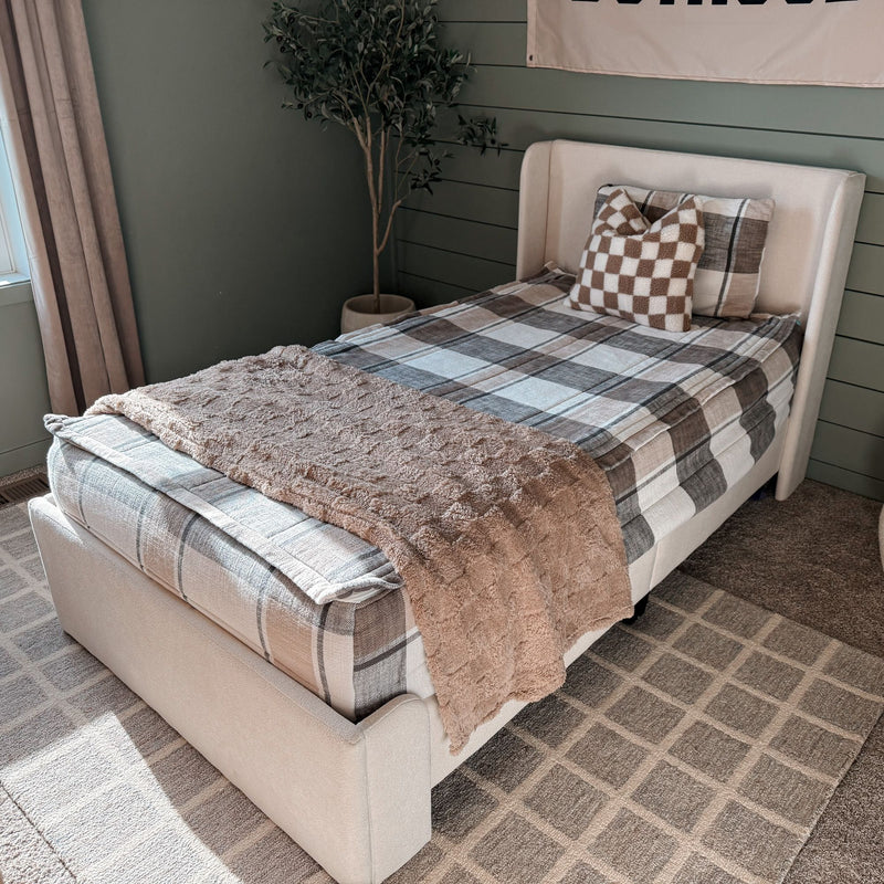 Cozy modern farmhouse twin bedroom with plaid bedding, neutral decor, beige faux fur throw, checkered pillow, green shiplap accent wall and potted indoor tree