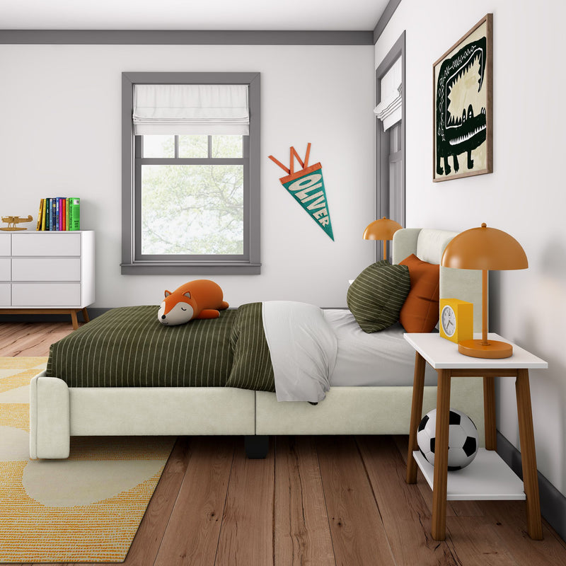 Modern children's bedroom with olive-green striped bedding, sleeping fox plush toy, orange bedside lamp, soccer ball, white dresser with colorful books, "Oliver" pennant and framed wall art