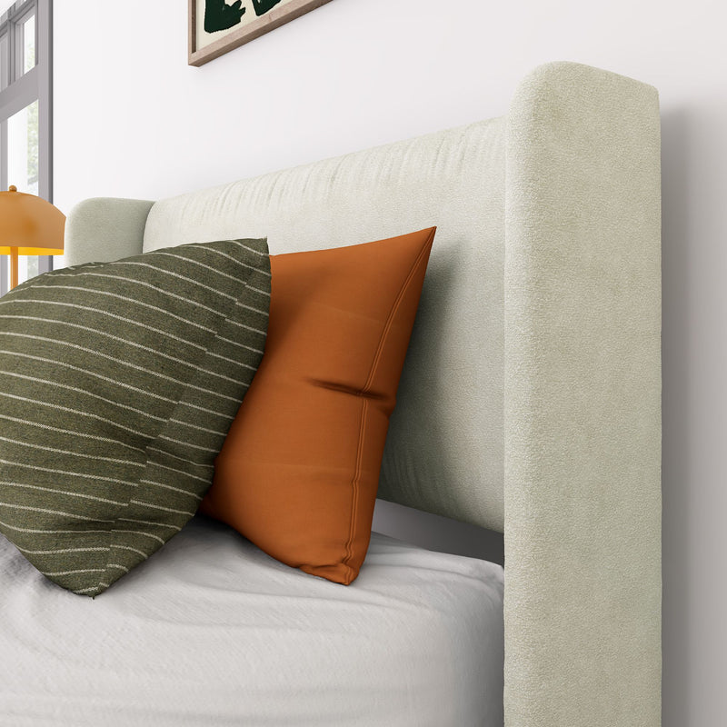 Close-up of beige upholstered headboard and modern bedroom decor with green striped and rust-orange throw pillows on white bedding, bedside lamp and window