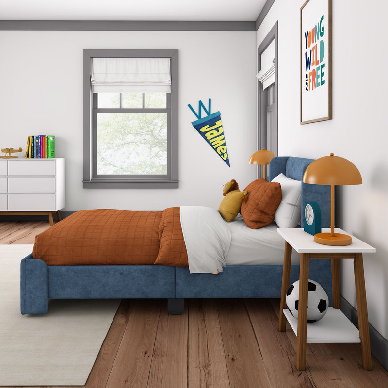 Modern kids bedroom decor with blue upholstered bed and orange bedding, stuffed lion, soccer ball, bedside lamp, pennant and colorful wall art