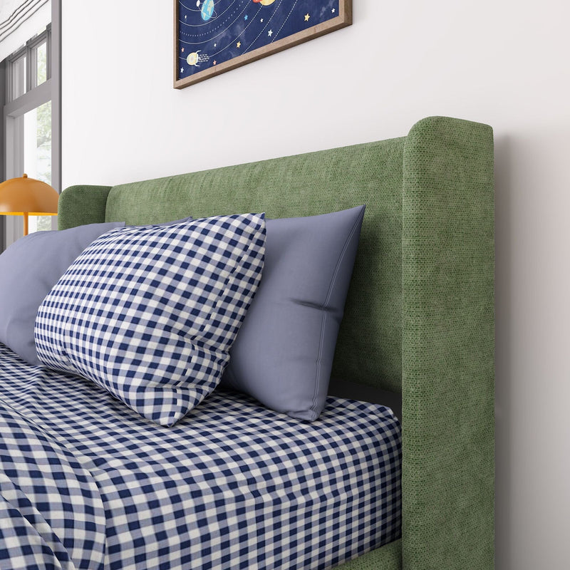 Green upholstered headboard with blue gingham bedding and light blue pillows in a modern bedroom with an orange bedside lamp and framed space artwork
