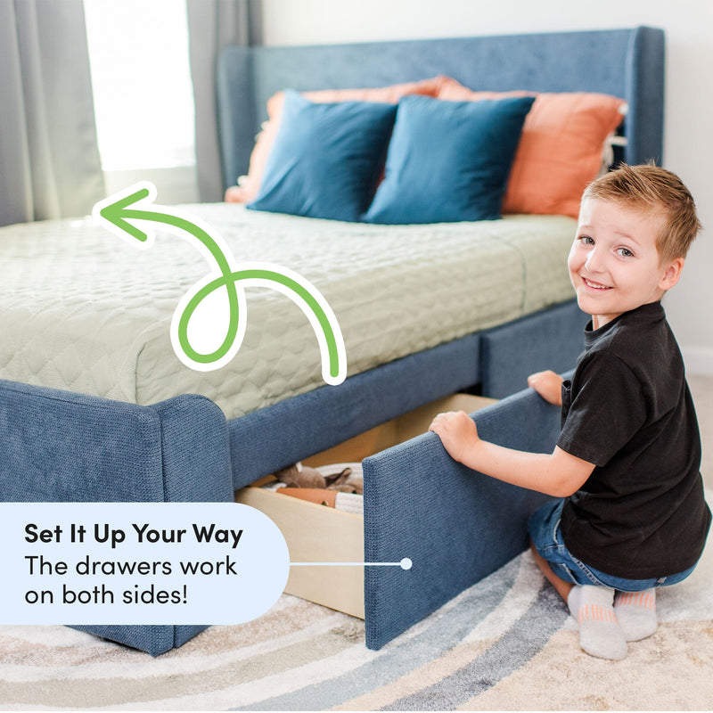 Child pulling out under-bed storage drawer from blue upholstered storage bed in bright kids' bedroom