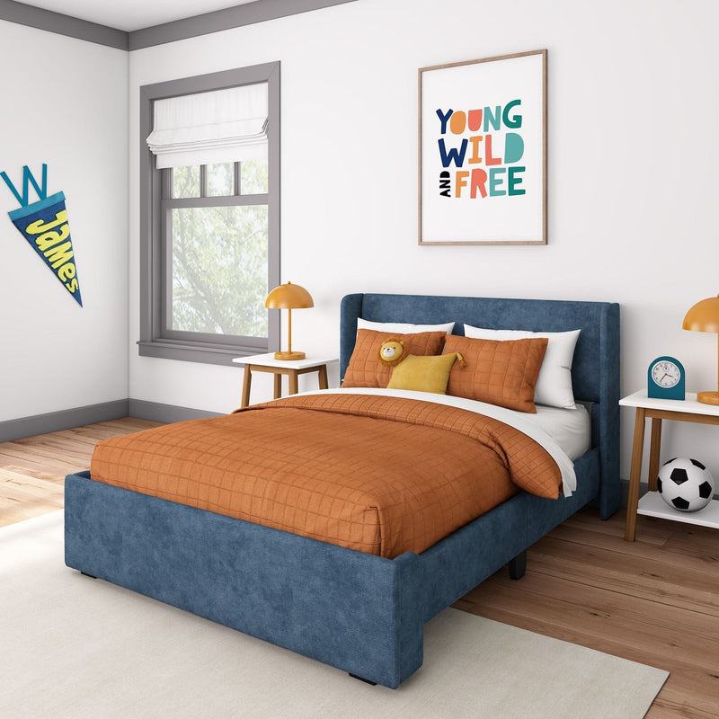 Modern kids bedroom with navy upholstered bed, orange quilted bedding, framed "Young Wild and Free" wall print, bedside lamp and soccer ball