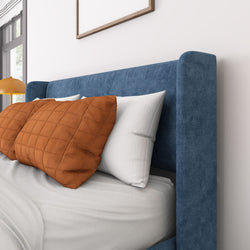 Blue upholstered bed with orange and white pillows in a modern bedroom setting.