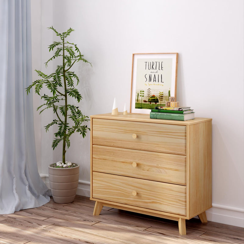 Minimalist light wood three-drawer dresser with mid-century legs styled in a Scandinavian nursery setting — potted green plant, framed "Turtle and Snail" children's print and stacked books on hardwood floor