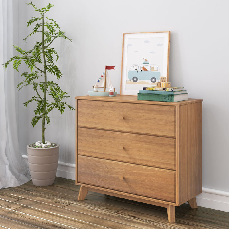 Mid-century modern three-drawer wooden dresser in bright nursery with potted plant, framed children's art, toy sailboat and stacked books on hardwood floor