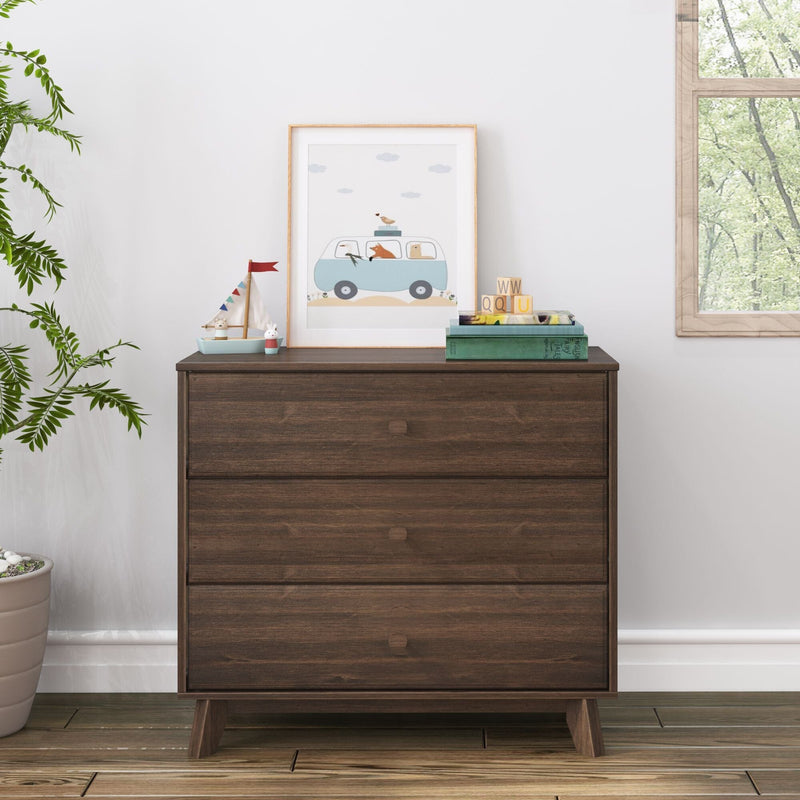 Dark wood mid-century three-drawer dresser in kids' nursery with framed animal car print, wooden toy boat, alphabet blocks and potted plant