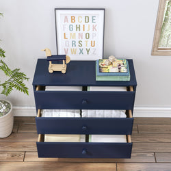Modern navy blue dresser with drawers open, displaying folded white linens, a wooden duck toy, and an alphabet print frame, perfect for a stylish nursery or kids' room.