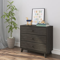 Dark wood dresser with three drawers in a modern nursery, featuring a potted plant, colorful alphabet art, and wooden toys on top.