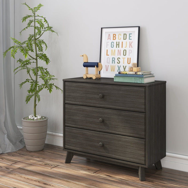 Mid-century dark gray three-drawer wooden dresser in nursery with colorful framed alphabet print, wooden toy horse, stacked books and potted plant